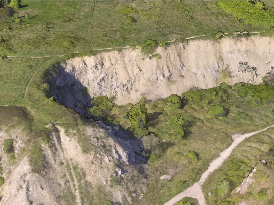 The quarry face seen at an angle from the south-west, built entirely of coloured points: pale rock, green scrub and trees, a footpath.